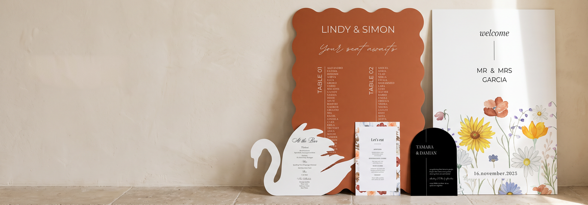 A coordinated wedding stationery set displayed on a stone floor against a textured beige wall.