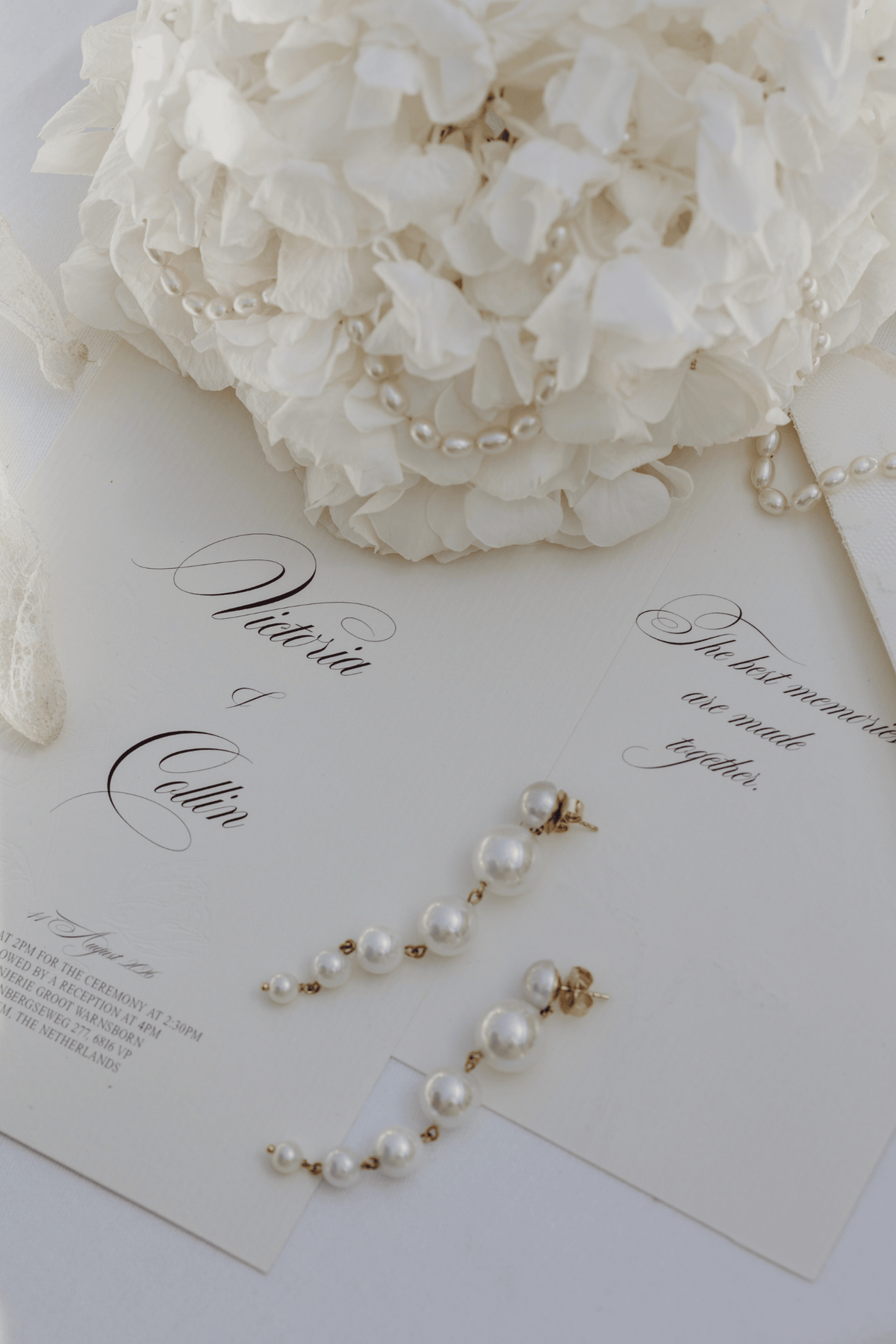 Pearl drop earrings with gold-toned posts and beads, arranged on wedding invitation cards beneath a white floral bouquet.