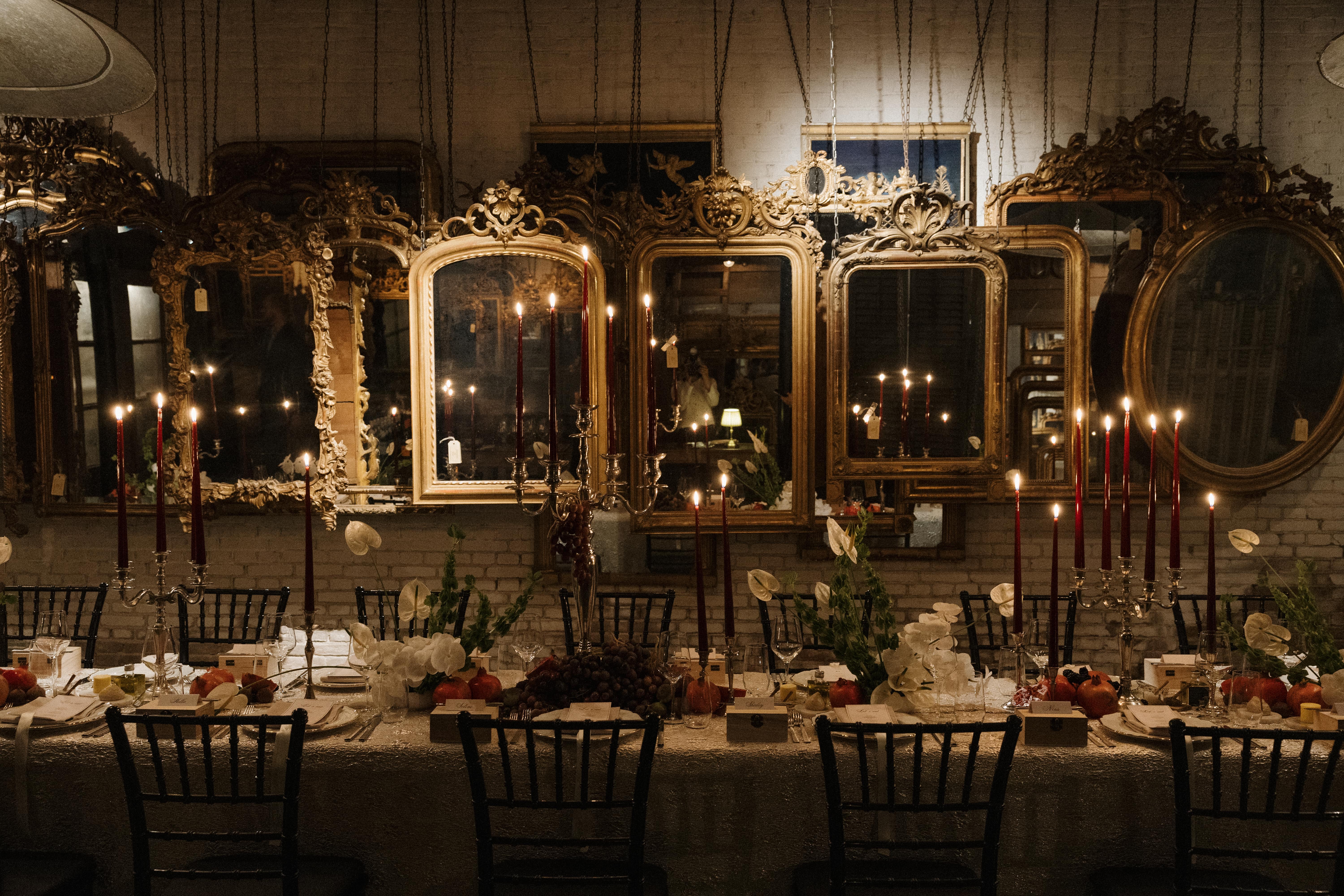 Elegant dining table setting with candles and mirrors in a dimly lit room.