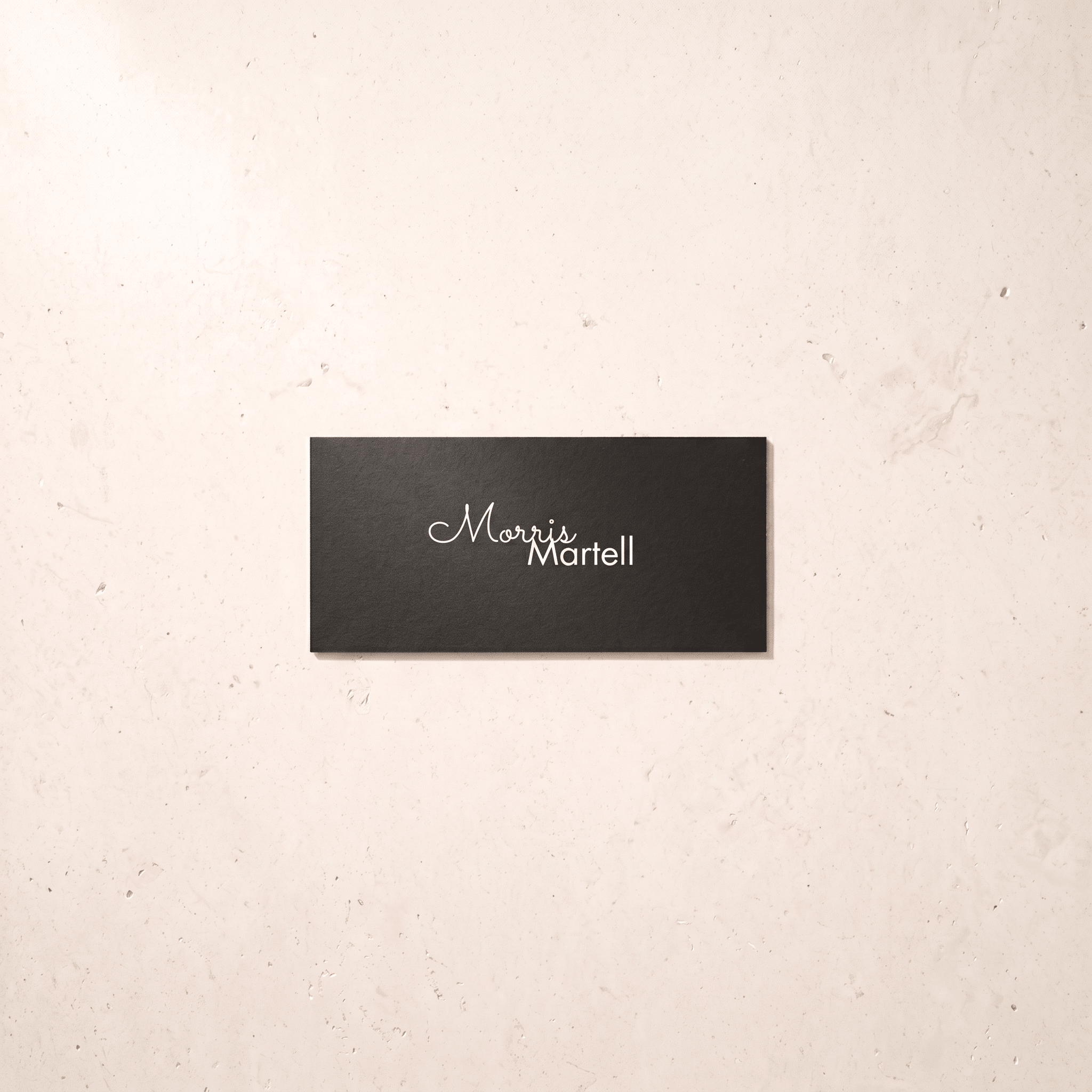 A rectangular black plaque with the name 'Morris Martell' in white script and serif lettering, mounted on a light beige textured wall.