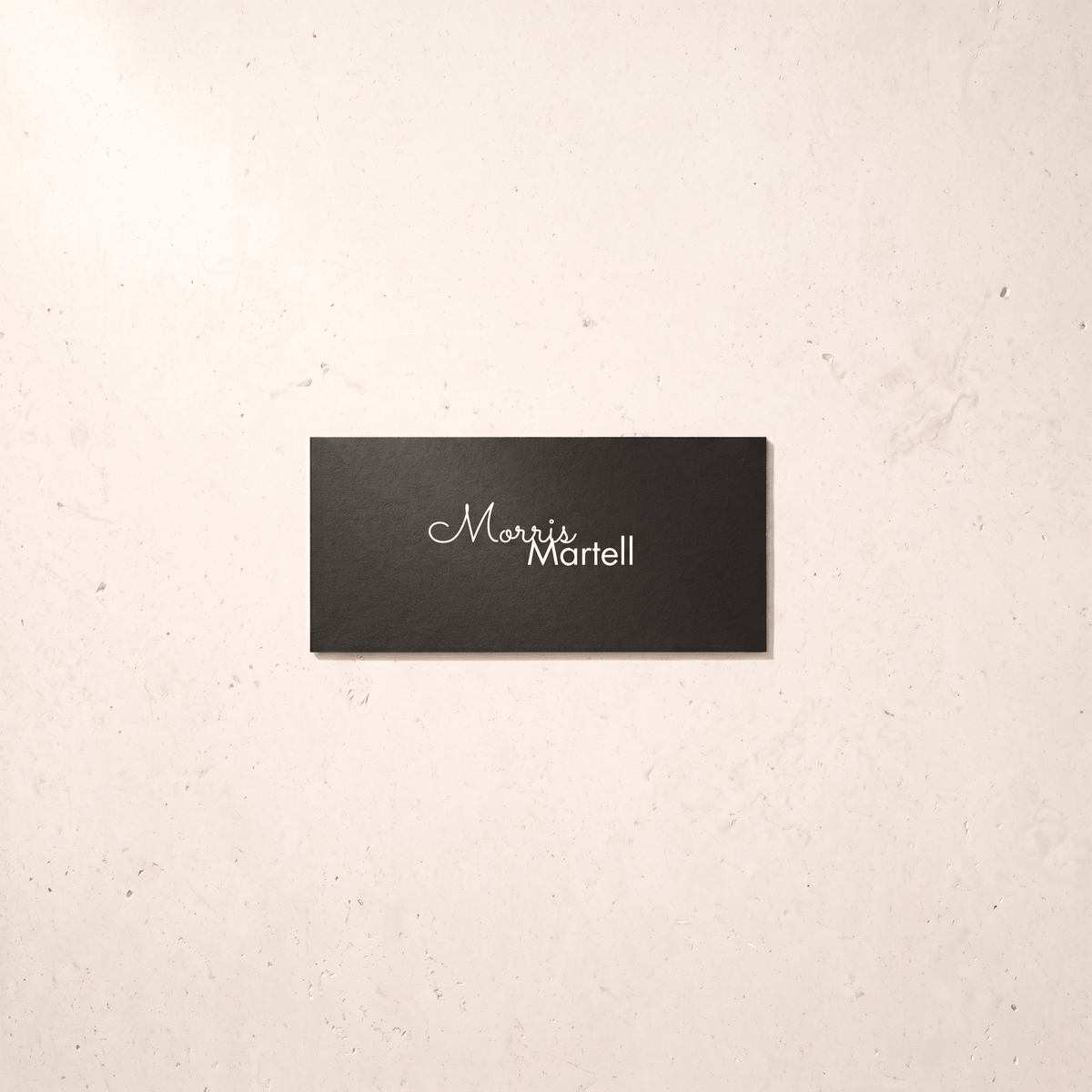 A rectangular black plaque with the name 'Morris Martell' in white script and serif lettering, mounted on a light beige textured wall.