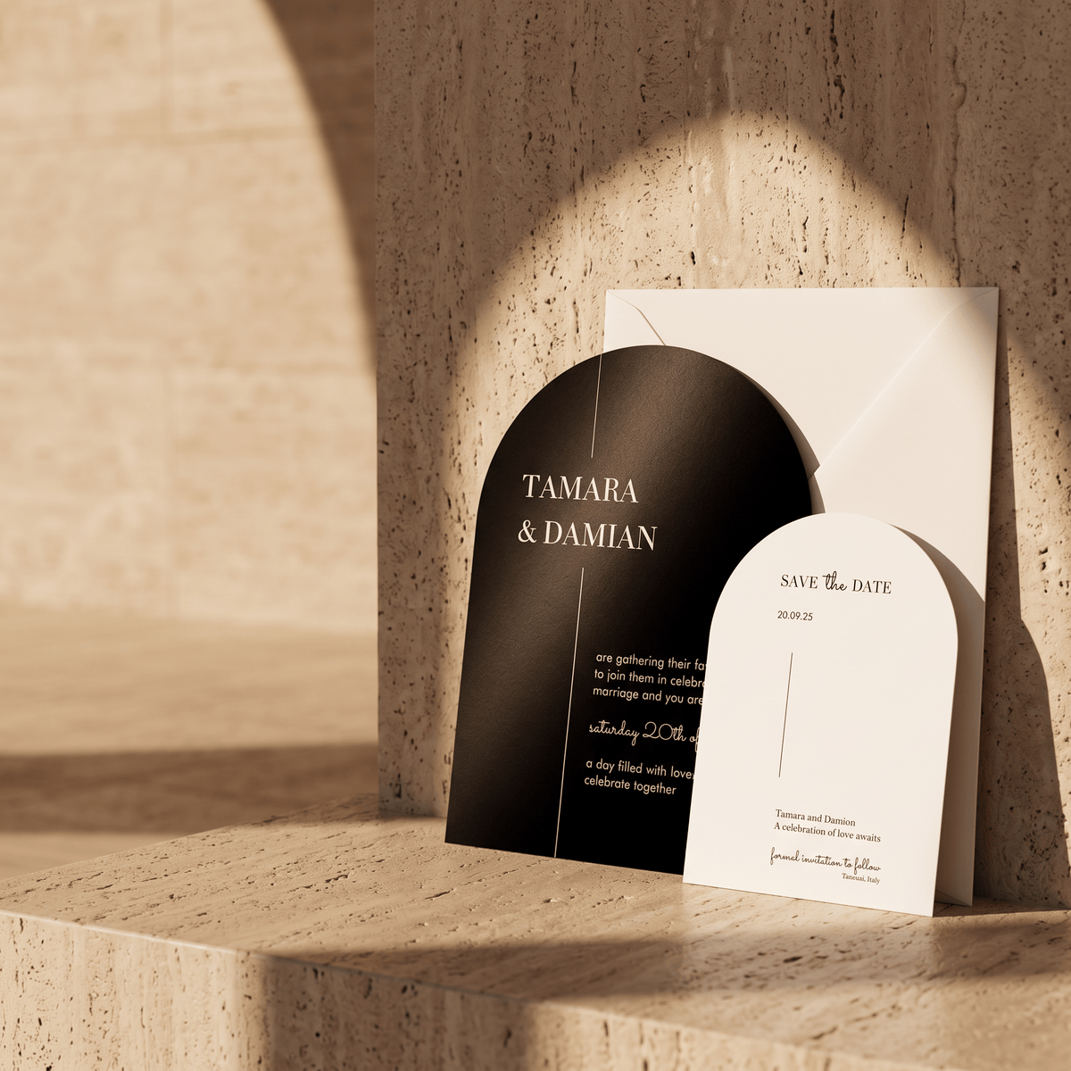Arch-shaped wedding invitation suite with a black and white design, displayed on a textured stone surface against a matching stone wall with dramatic warm sunlight and shadows.