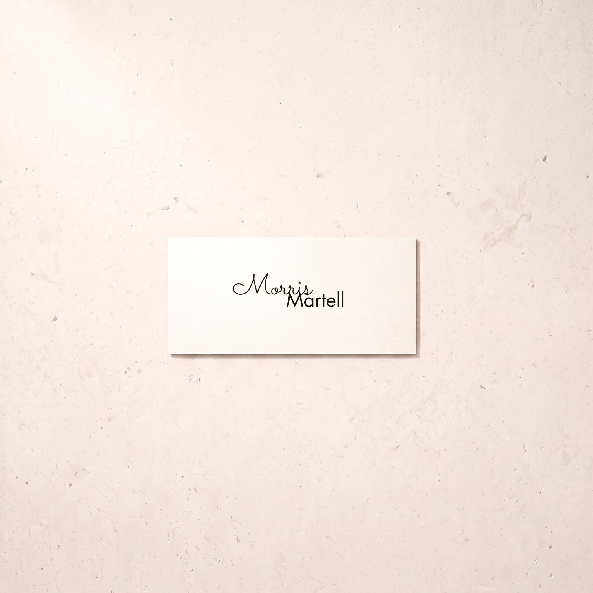 A small white rectangular card with the printed name 'Mavis Martell' in black script and sans-serif lettering, placed on a light beige textured surface.