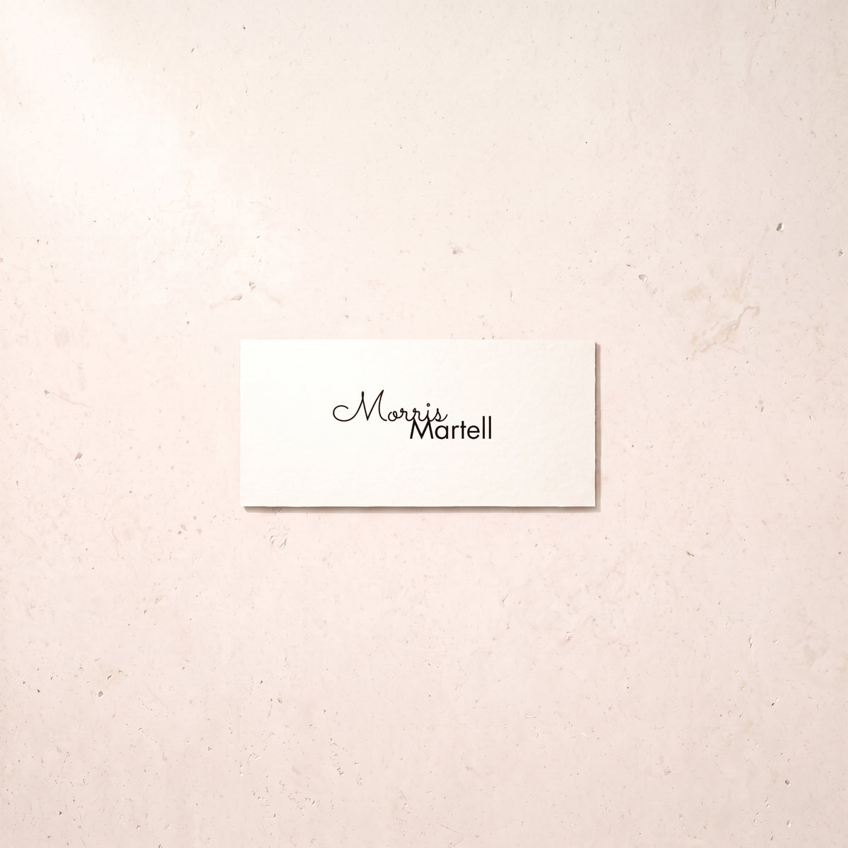 A small white rectangular card with the printed name 'Mavis Martell' in black script and sans-serif lettering, placed on a light beige textured surface.