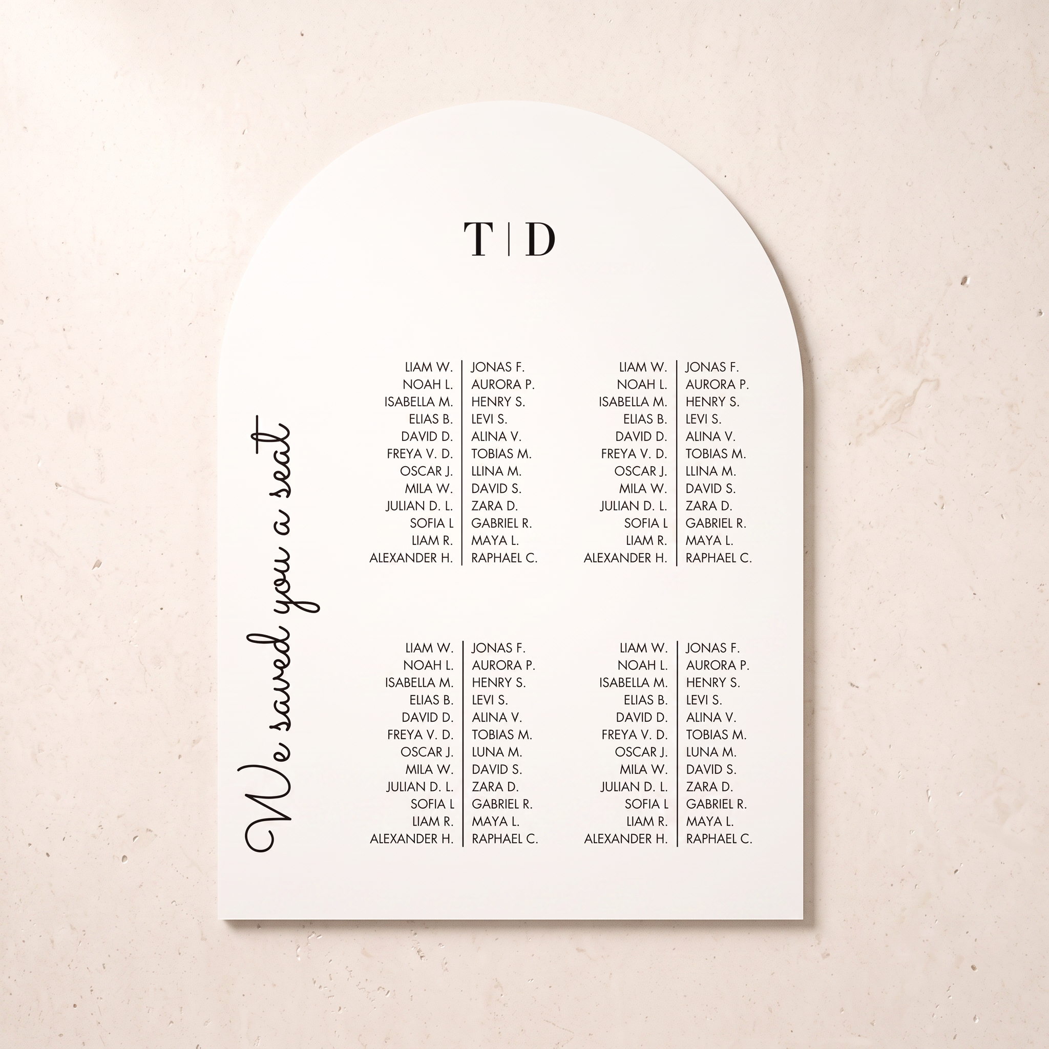 An arched white wedding seating card with black printed text, featuring the heading 'T | D' at the top, a list of names under that heading, and the phrase 'We saved you a seat' in script on the left side, photographed on a light beige textured background.