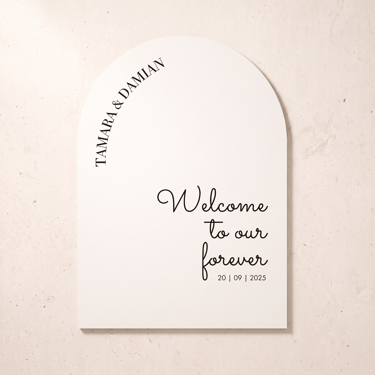 A personalized tombstone-shaped wedding sign with an arched top, printed with the names 'TAMARA & DAMIAN' and the phrase 'Welcome to our forever 20 | 09 | 2025' in black text on a warm off-white background, shown against a light beige textured wall.