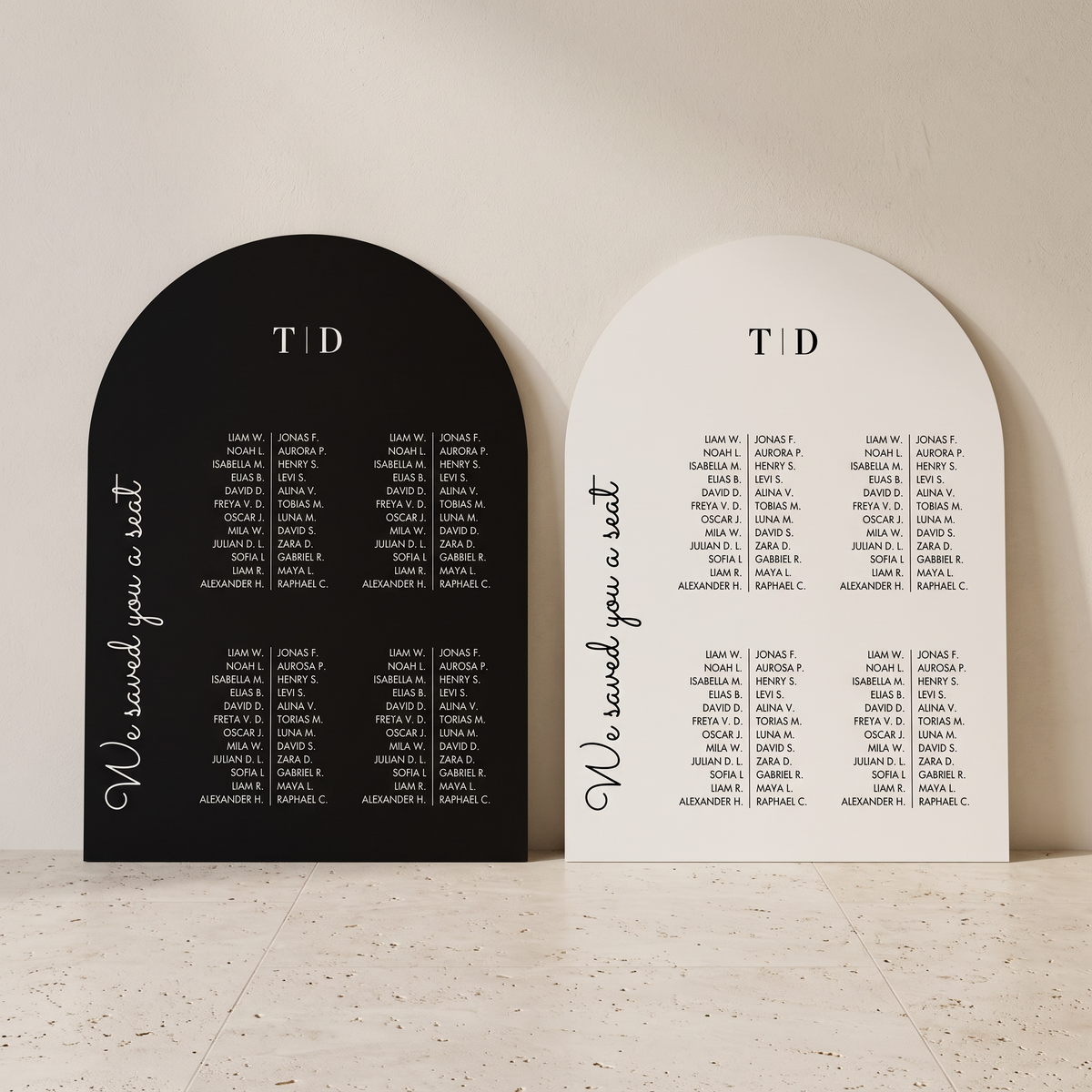 Two arched wedding seating cards displayed side by side on a light stone surface against a beige wall. One card is black with white text reading 'We send you a seat' and the names of guests, with 'T&D' at the top.