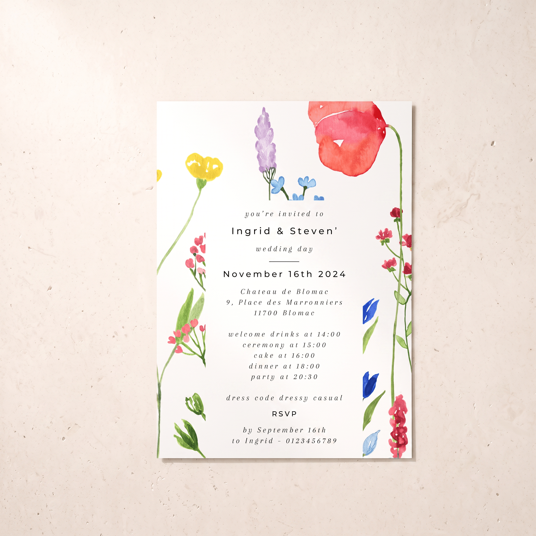 A vertical wedding invitation card with a white background and colorful watercolor floral illustrations, photographed against a light beige textured wall.