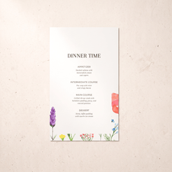 A vertical wedding dinner time menu card with elegant black typography on a white background, decorated with colorful watercolor floral illustrations at the bottom and right edge, displayed on a textured light beige surface.
