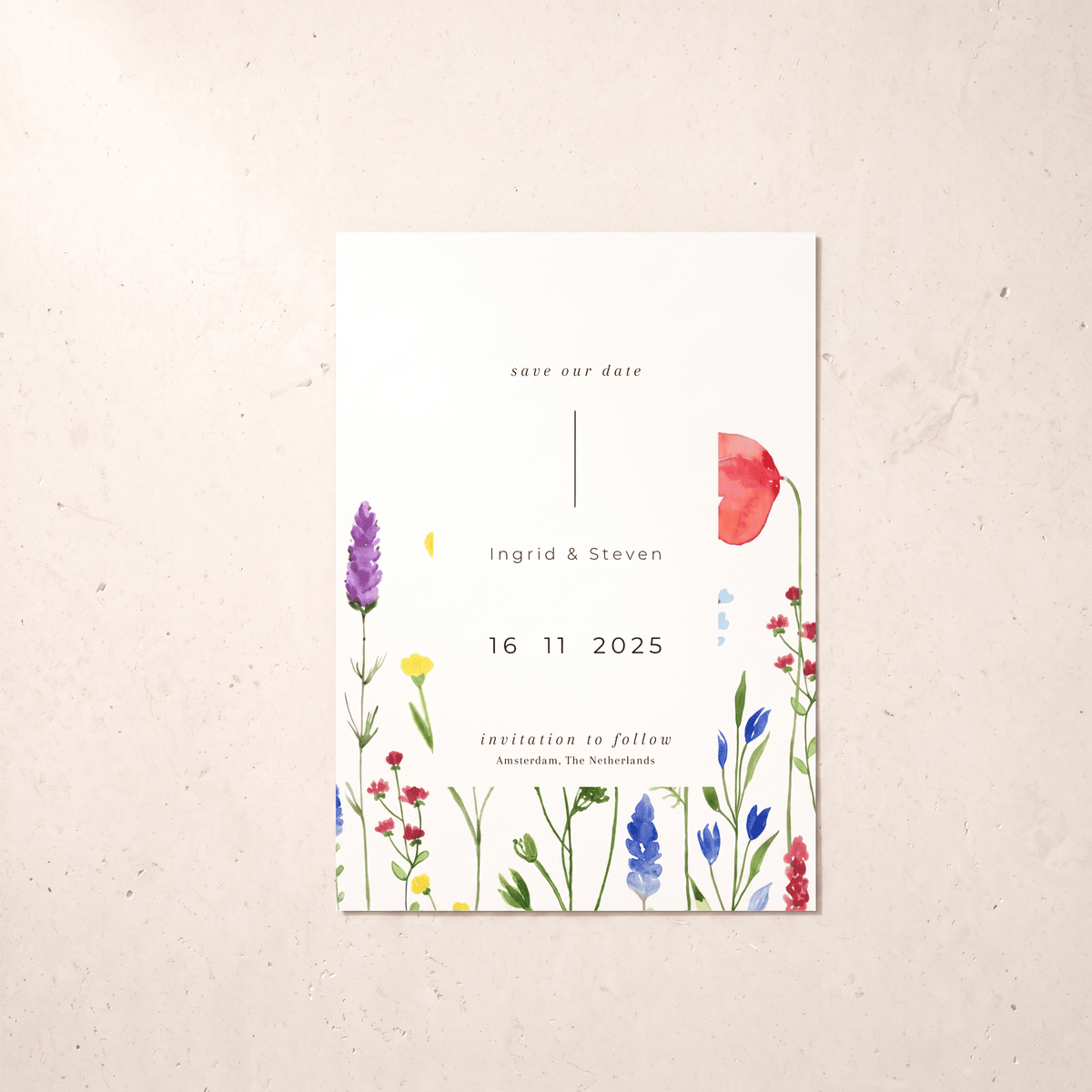 A vertical white save-the-date card with watercolor wildflower illustrations in red, purple, blue, yellow, and green, placed on a light beige textured surface.