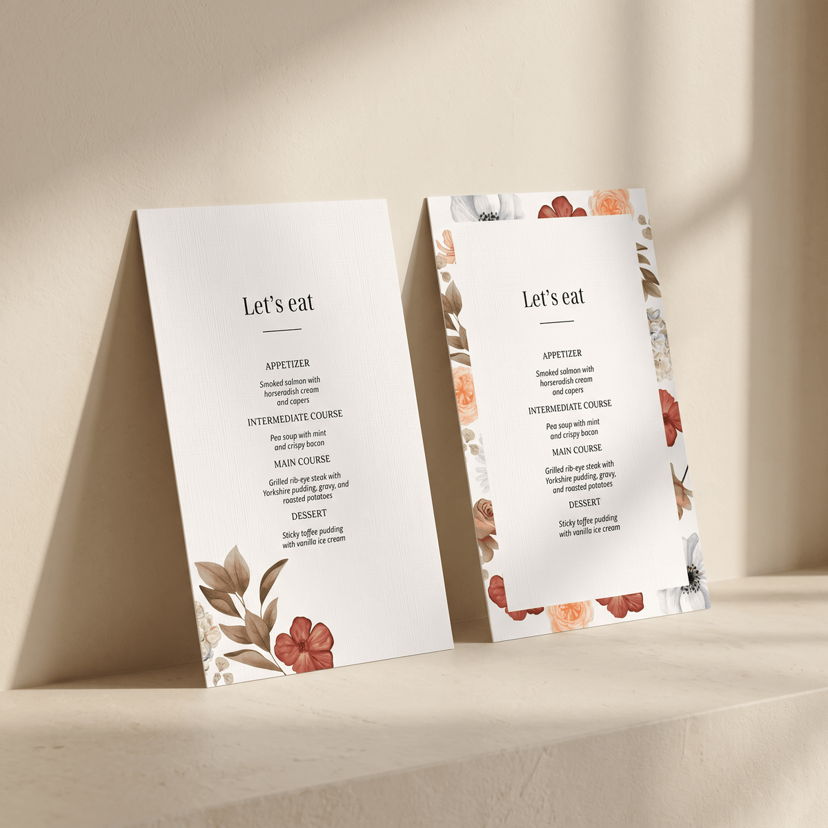 Two elegant wedding program or menu cards with floral illustrations, standing upright on a beige stone surface against a matching background.
