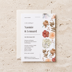 A floral wedding invitation card with a matching envelope, styled flat-lay on a textured beige stone surface. The card features elegant typography and a watercolor-style floral design on the right side in soft peach, pink, cream, and muted green tones.