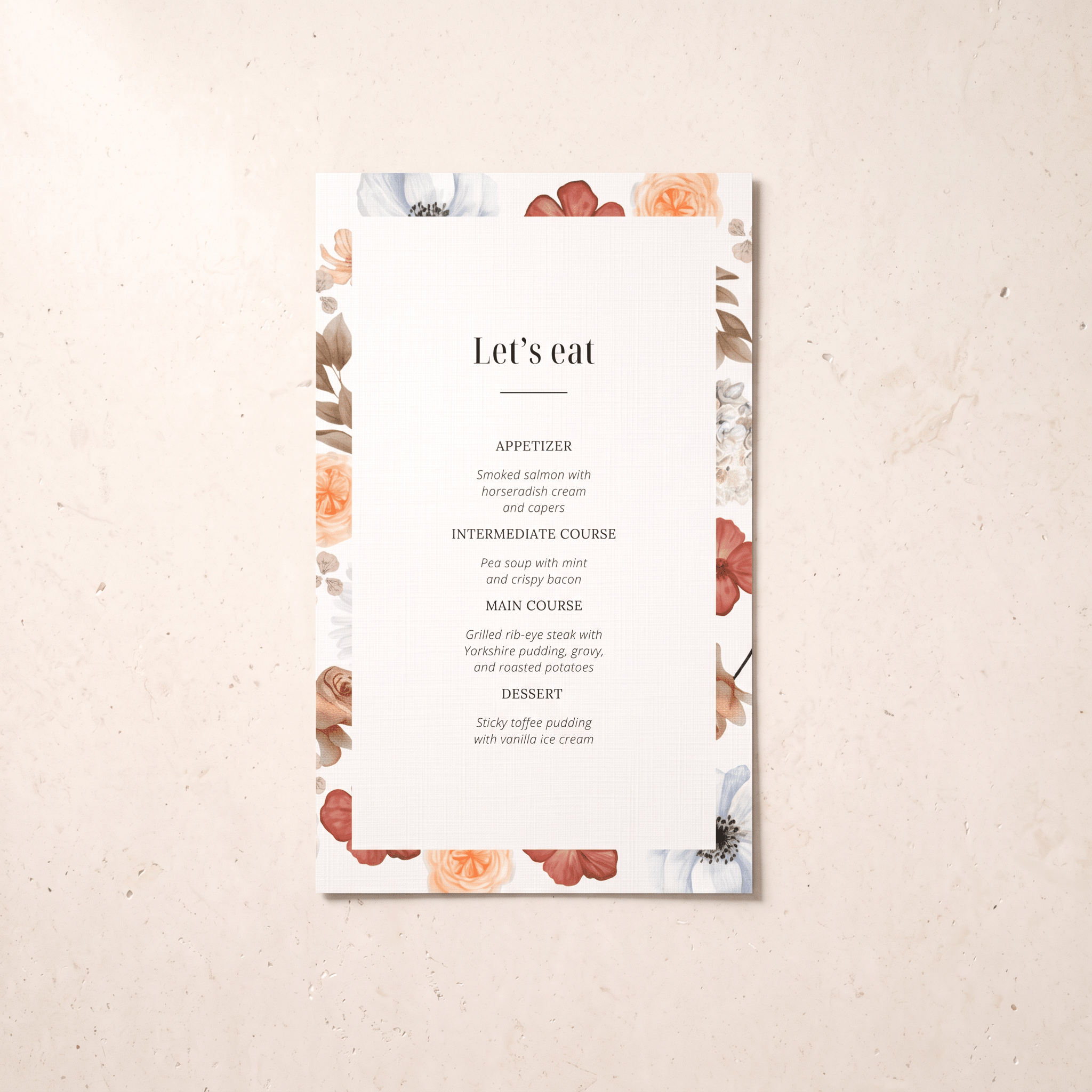 A vertical wedding menu card with a white center and a floral border in muted peach, dusty rose, and sage tones, photographed on a light beige textured surface. The printed text reads “Let’s eat” with course suggestions below.