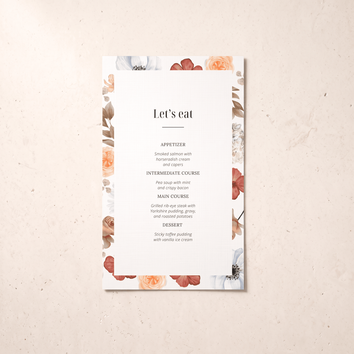 A vertical wedding menu card with a white center and a floral border in muted peach, dusty rose, and sage tones, photographed on a light beige textured surface. The printed text reads “Let’s eat” with course suggestions below.