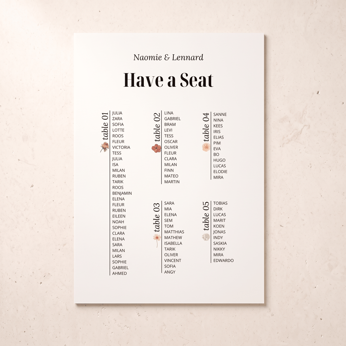 A vertical white wedding seating chart print with the names 'Naomie & Lennard' at the top and columns labeled table 01 through table 05, photographed against a light beige textured background.
