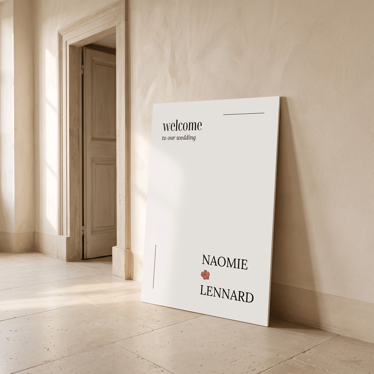 A large white personalized wedding welcome sign leaning against a beige plaster wall in a sunlit room. The sign reads 'welcome to our wedding' with the names 'NAOMIE' and 'LENNARD' separated by a small red rose icon.