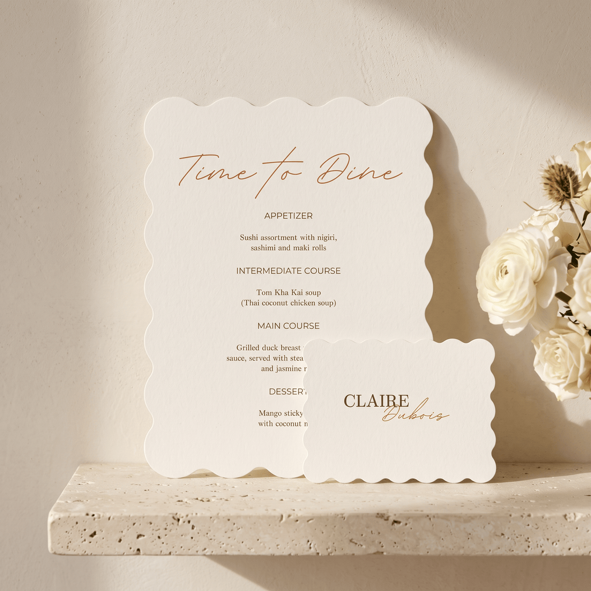 A scalloped cream paper menu card with elegant copper-gold typography reading 'Time to Dine' and course details, styled on a stone ledge beside white flowers against a warm beige wall.