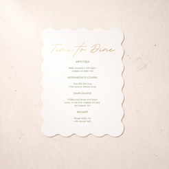 A scalloped white paper menu card with elegant gold foil text reading 'Time to Dine' and black printed meal options, placed on a light beige textured surface.