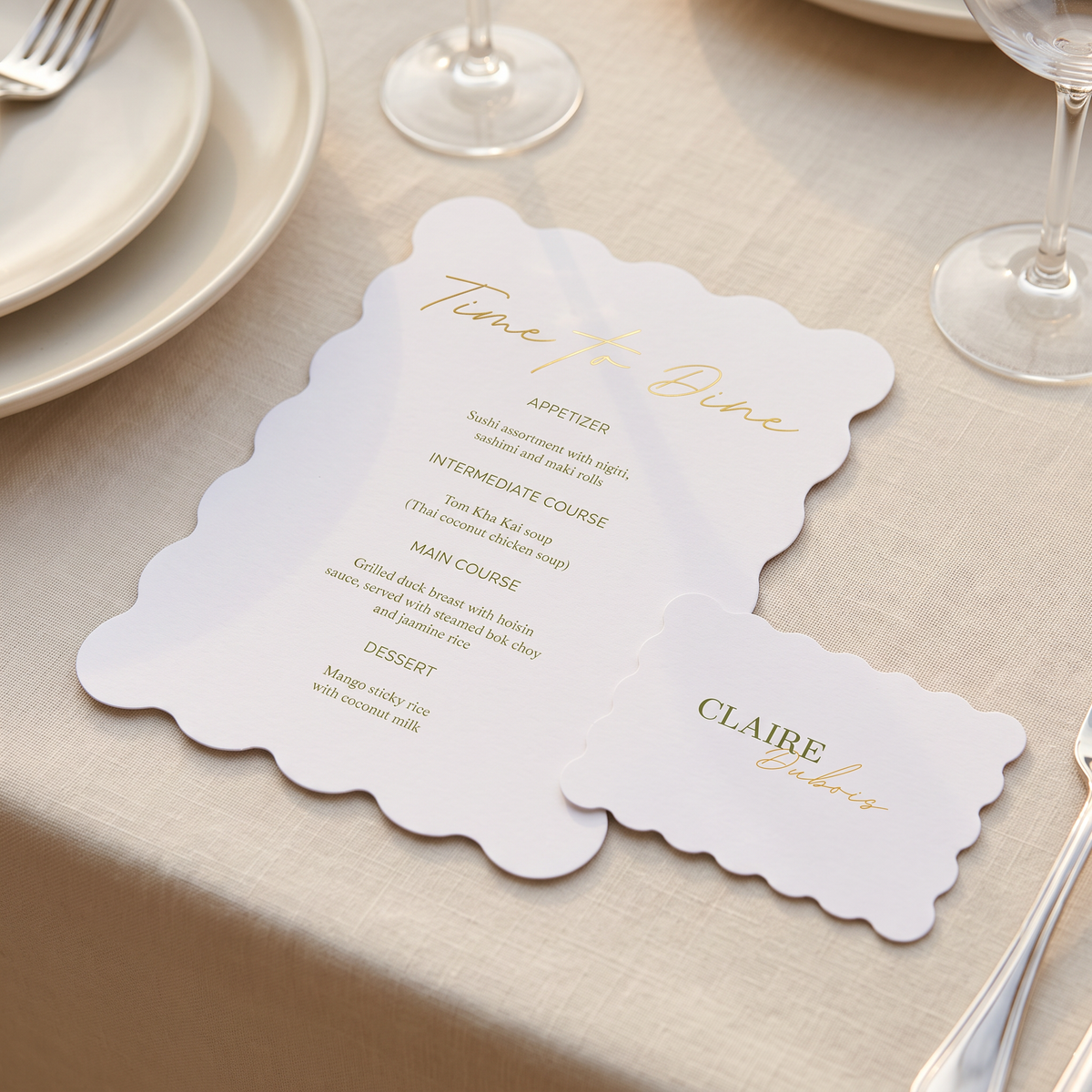 A scalloped white wedding table card set on a beige tablecloth, featuring elegant gold script text and printed course details for a dinner party.