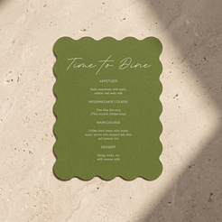 An olive green scalloped-edge menu card reading 'Time to Dine' with course text below, placed on a light beige stone surface with soft shadows.