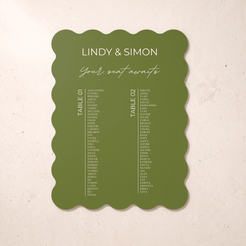 An olive green scalloped-edge wedding seating card with white text reading 'LINDY & SIMON Your seat awaits' and two columns of guest names, photographed against a light beige textured background.