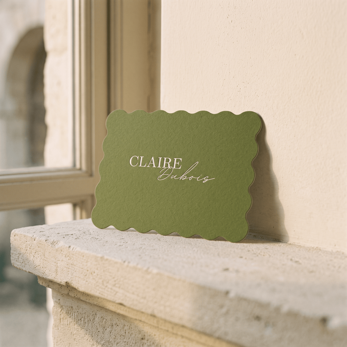 A scalloped sage green card with the text 'CLAIRE Habits' in white, leaning against a beige wall on a stone windowsill.