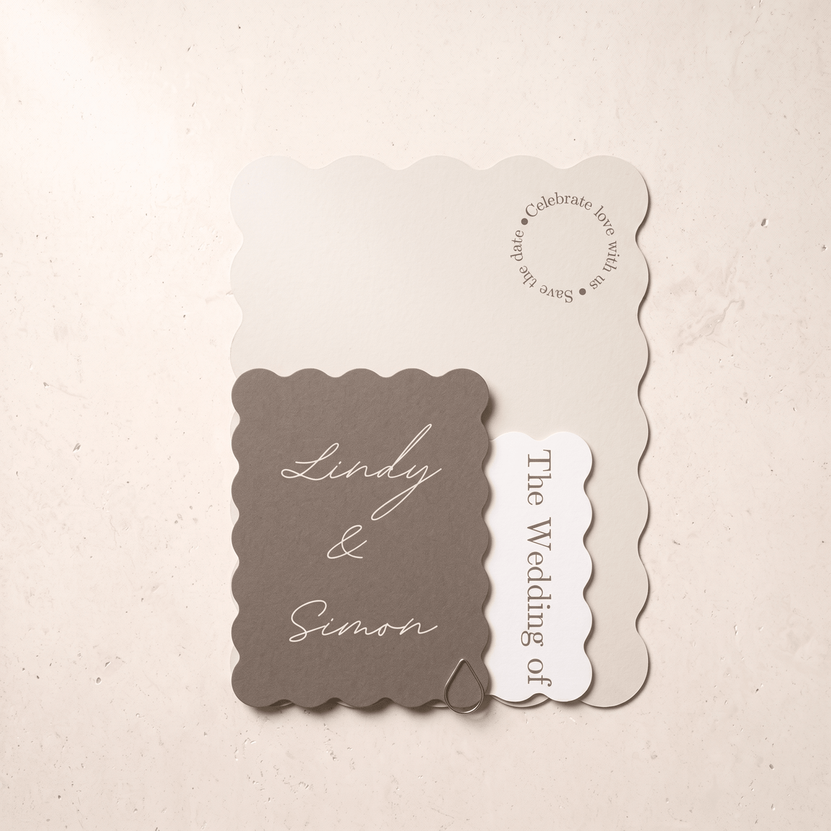 A wedding invitation suite featuring a taupe scalloped card with 'Lindy & Simon' in white script, layered over a cream card that reads 'Celebrate love with us' and a small white tag reading 'The Wedding of'.