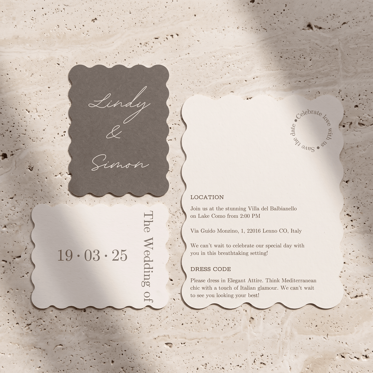 A wedding invitation suite featuring a scalloped-edge card set in taupe and cream, laid flat on a textured beige stone surface. The suite includes a taupe card with white script reading 'Lindy & Simon,' a cream card with event details, and a matching cream date stamp.