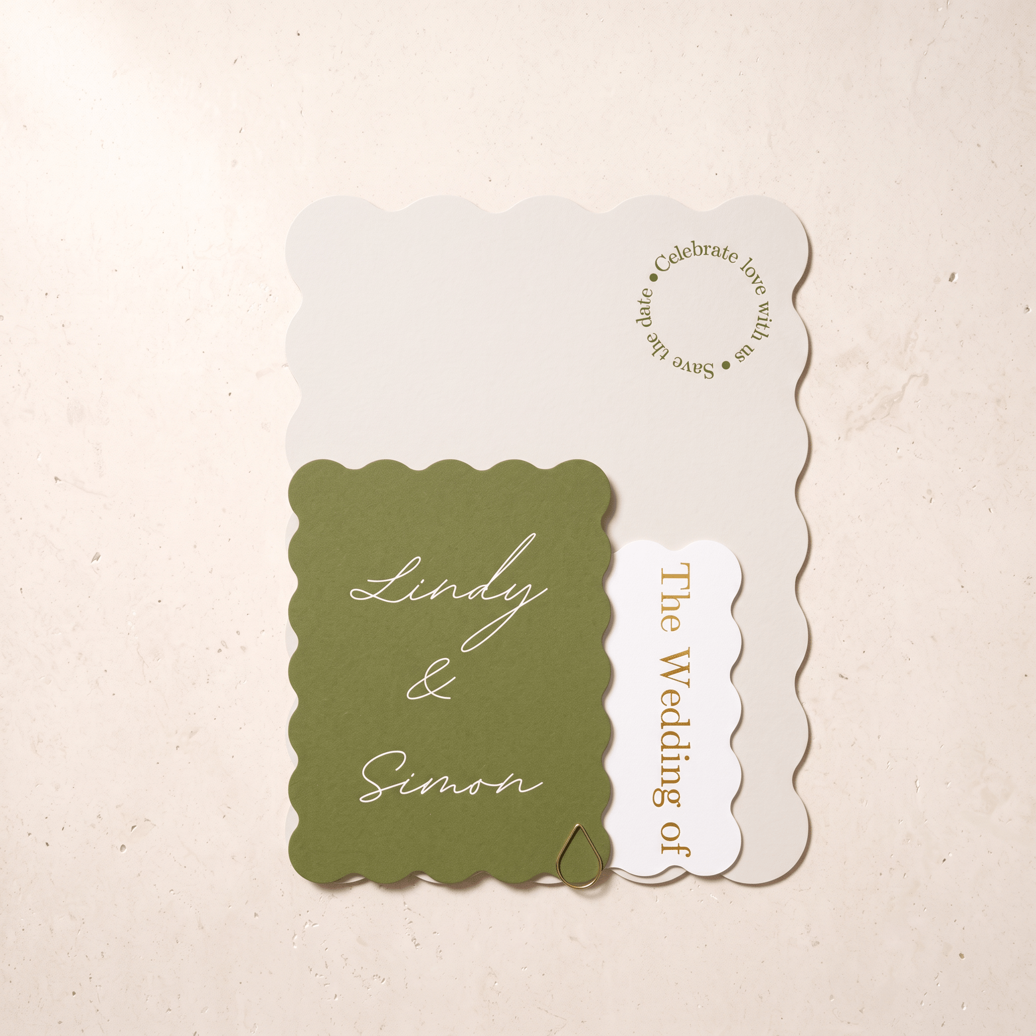 A wedding invitation suite featuring a scalloped olive green card with white script reading 'Lindy & Simon,' a white scalloped card with gold text reading 'The Wedding of,' and a larger off-white invitation background card with gold text, arranged on a light beige textured surface.