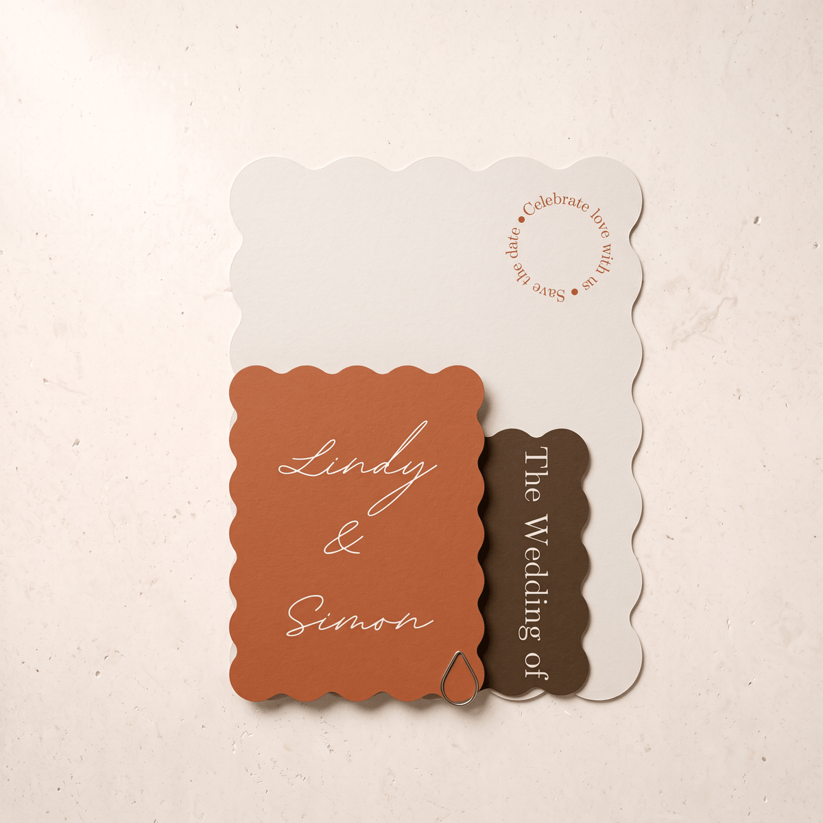 A set of scalloped-edge wedding invitation cards arranged on a light beige textured surface. The set includes an off-white card with a circular save-the-date message, a terracotta orange card with the names 'Lindy & Simon' in white script, and a dark brown card reading 'The Wedding of'.