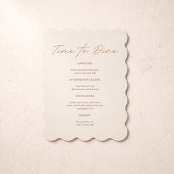 A scalloped cream paper menu card with orange script and black text reading 'Time to Dine' and course listings, placed on a light beige textured surface.