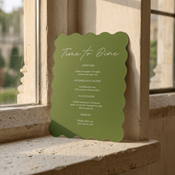 A green scalloped-edge menu card titled "Time to Dine" leaning against a stone window sill in warm natural light.