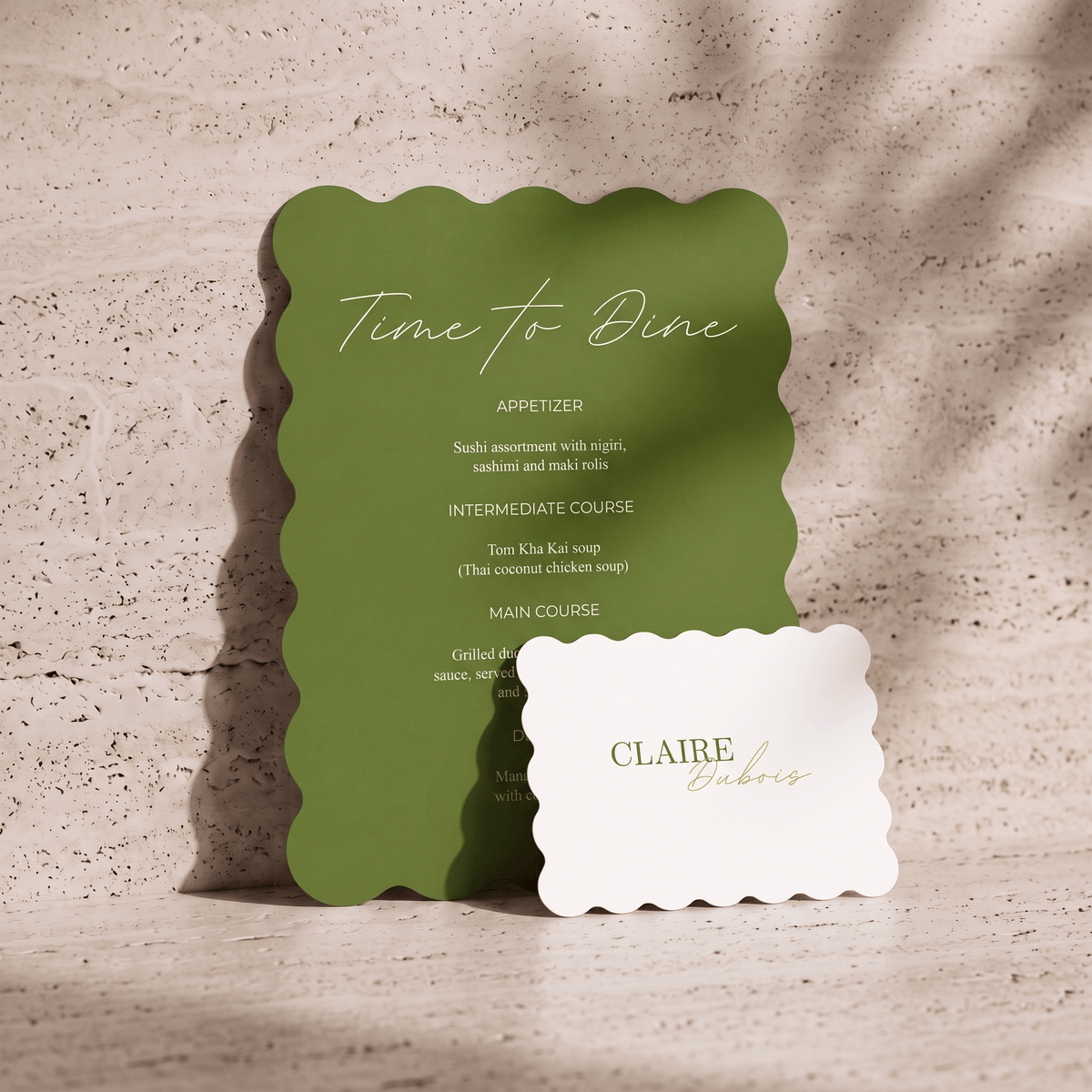A green scalloped-edge restaurant menu card standing on a stone surface, with a white scalloped-edge name card in front reading 'CLAIRE bistro.'.