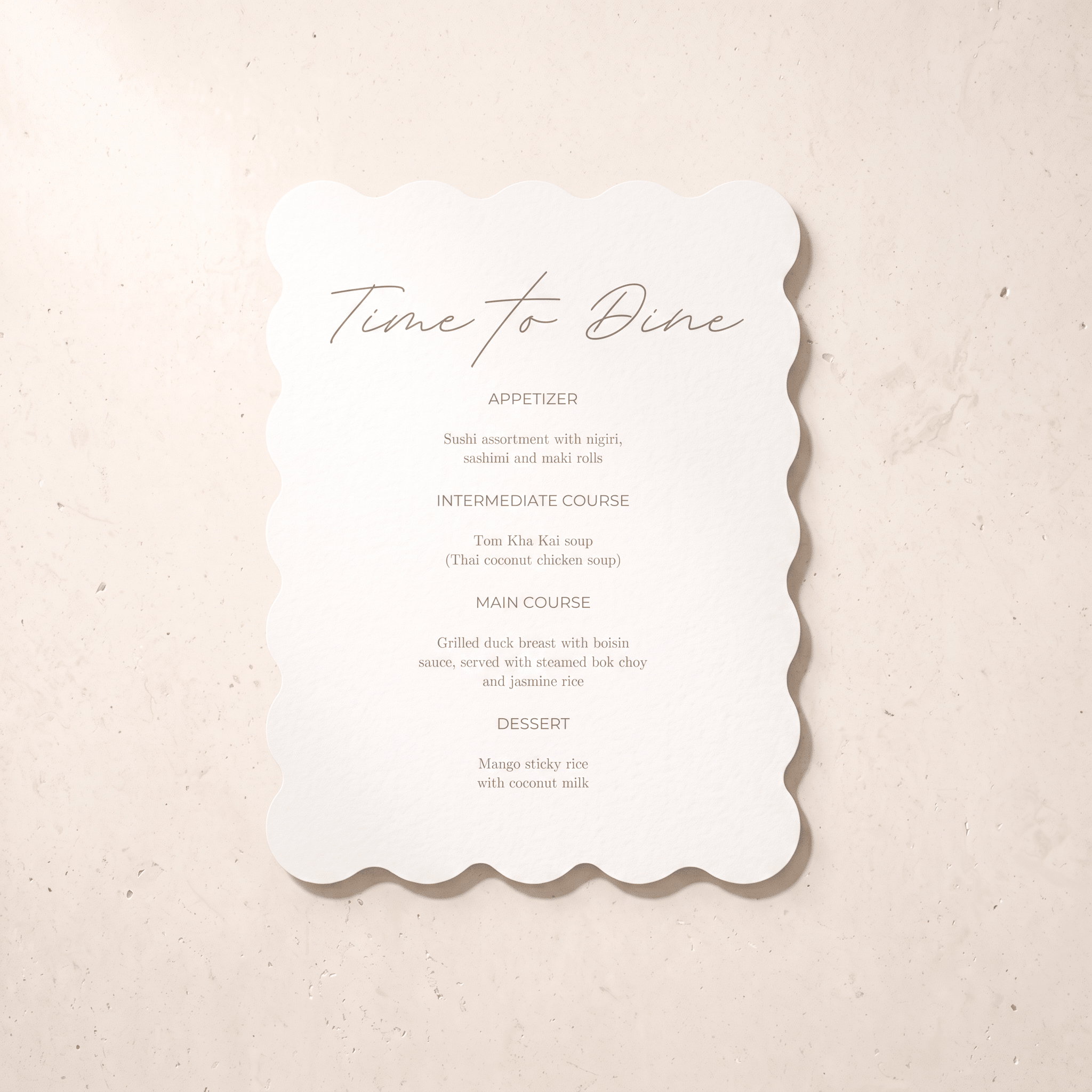 A scalloped white paper dinner menu card with elegant script and course text, photographed flat on a light beige textured surface.