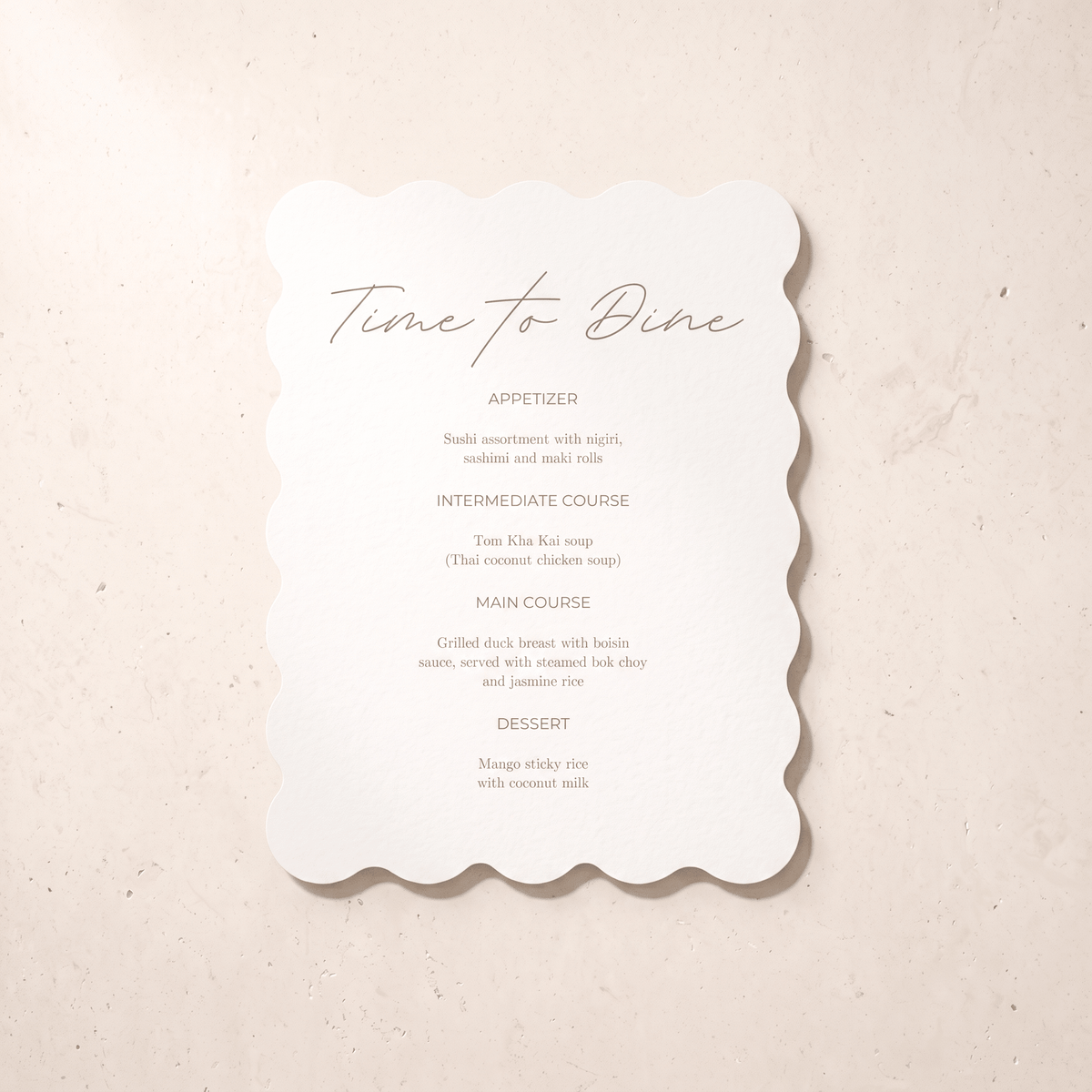 A scalloped white paper dinner menu card with elegant script and course text, photographed flat on a light beige textured surface.