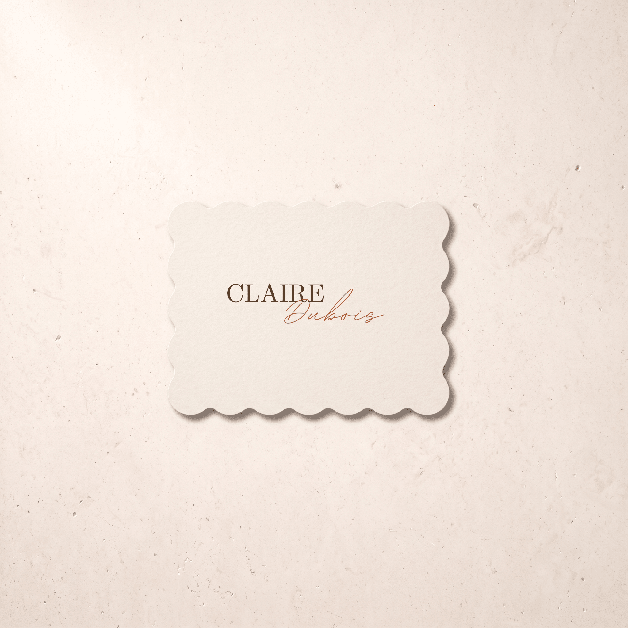A scalloped-edge cream card with the text 'CLAIRE Euboris' in brown and copper script, centered on a textured beige background.