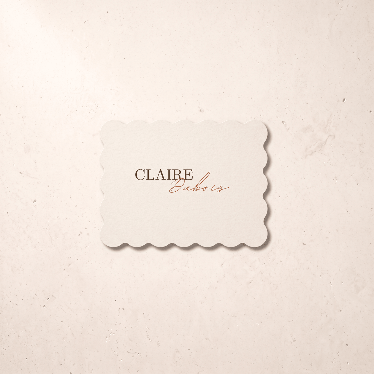 A scalloped-edge cream card with the text 'CLAIRE Euboris' in brown and copper script, centered on a textured beige background.