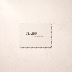 A scalloped-edge cream card with the text 'CLAIRE Euboris' in brown and copper script, centered on a textured beige background.