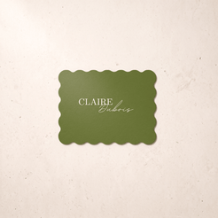A rectangular green-colored card with scalloped edges and the text 'CLAIRE Dubois' in white, centered on a textured cream background.