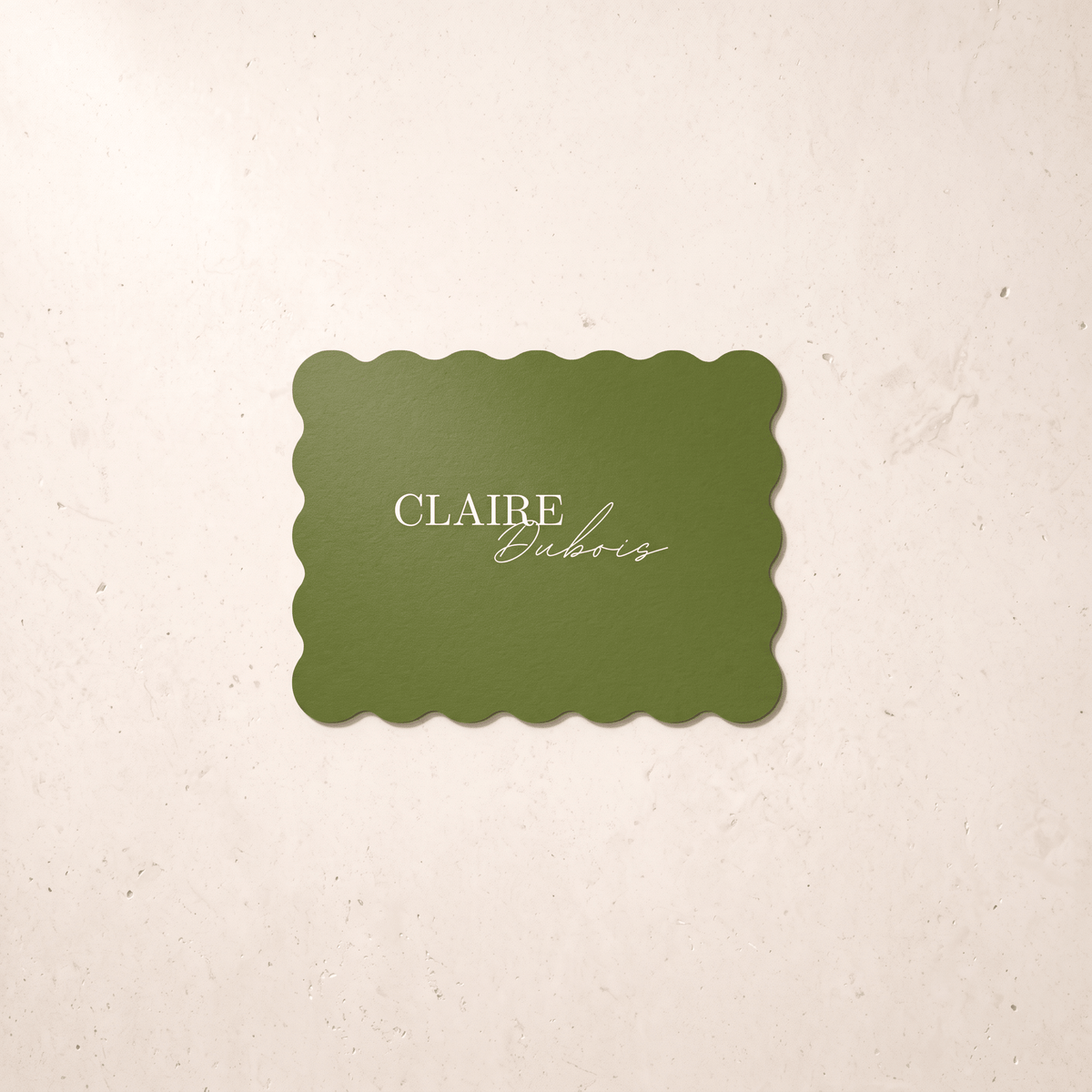 A rectangular green-colored card with scalloped edges and the text 'CLAIRE Dubois' in white, centered on a textured cream background.