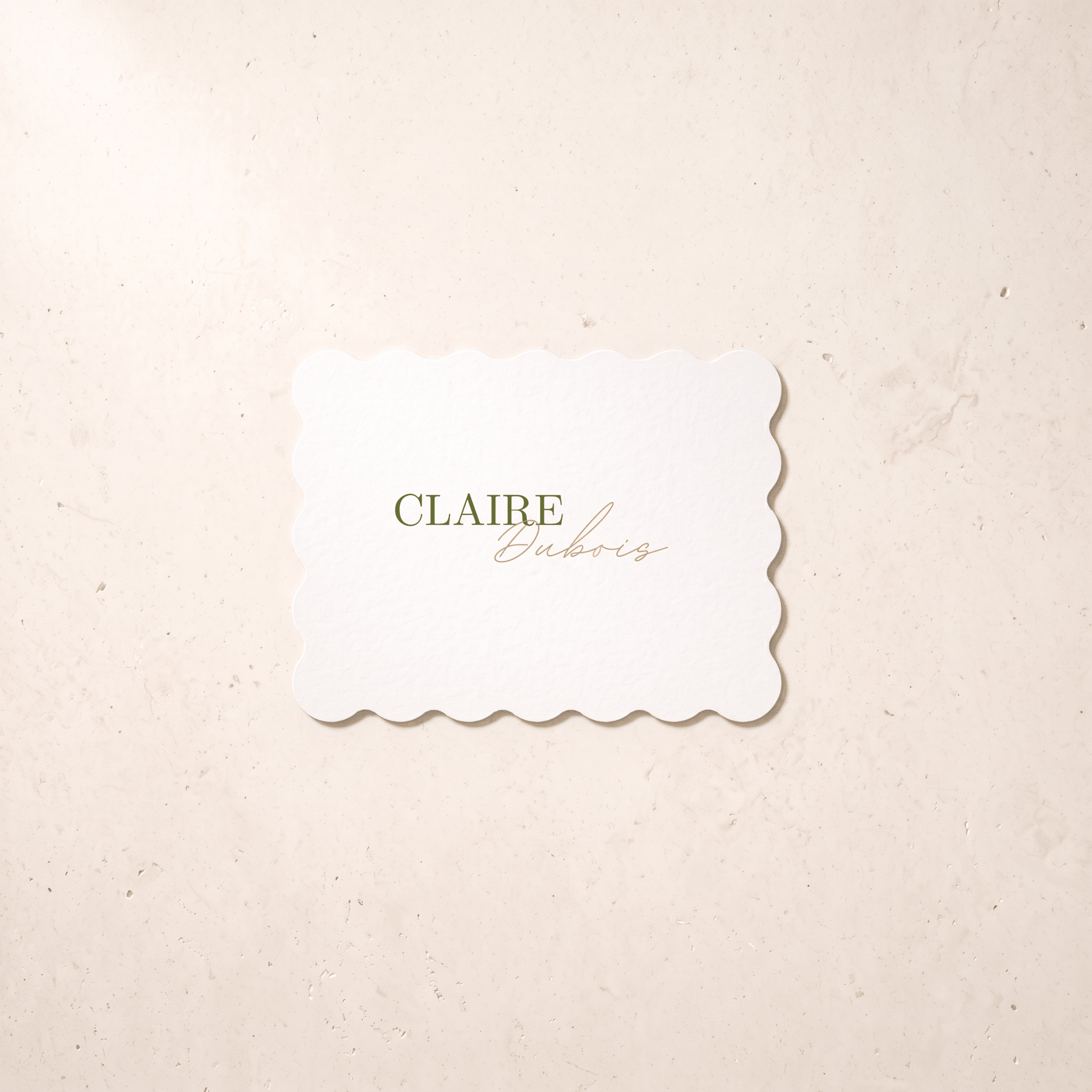 A rectangular white-colored card with scalloped edges and the text 'CLAIRE Dubois' in green and gold, centered on a textured cream background.