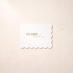 A rectangular white-colored card with scalloped edges and the text 'CLAIRE Dubois' in green and gold, centered on a textured cream background.