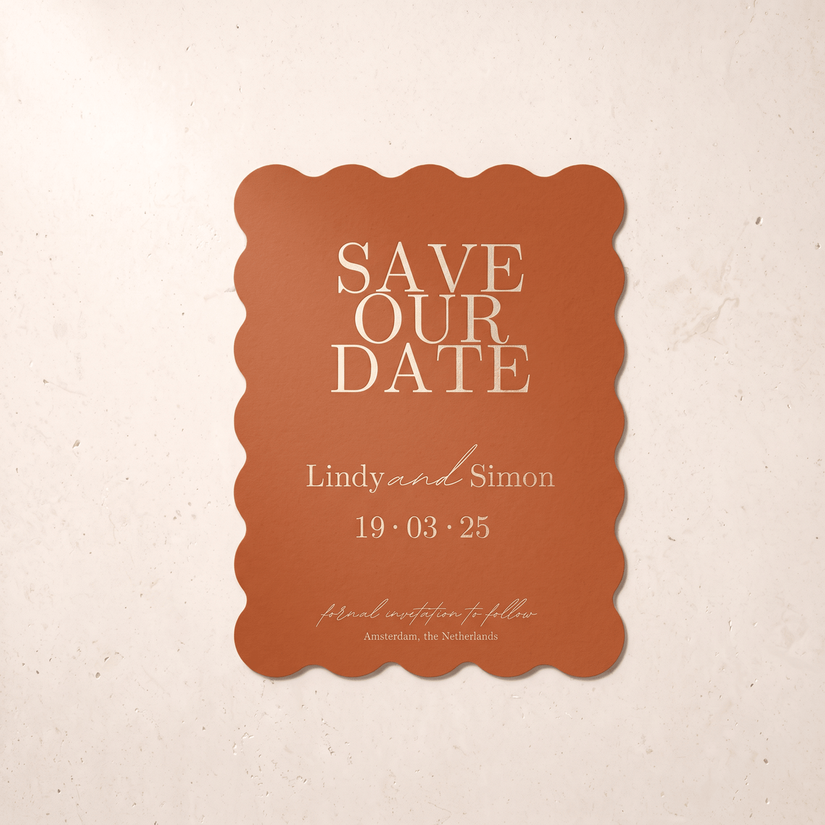 A terracotta-colored scalloped 'Save Our Date' card with gold typography, displayed against a textured beige background.