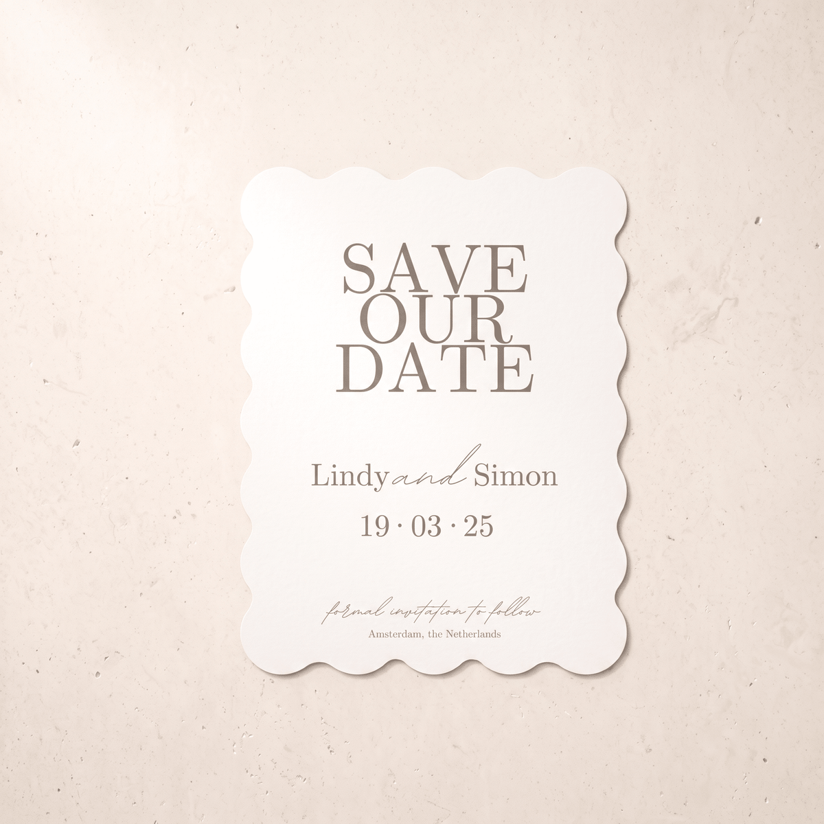 A scalloped white 'Save Our Date' card with gray text, displayed flat on a textured beige background.