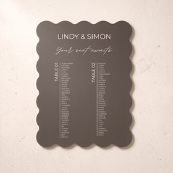 A scalloped anthracite wedding seating card with white printed text, displayed flat against a light beige textured background.
