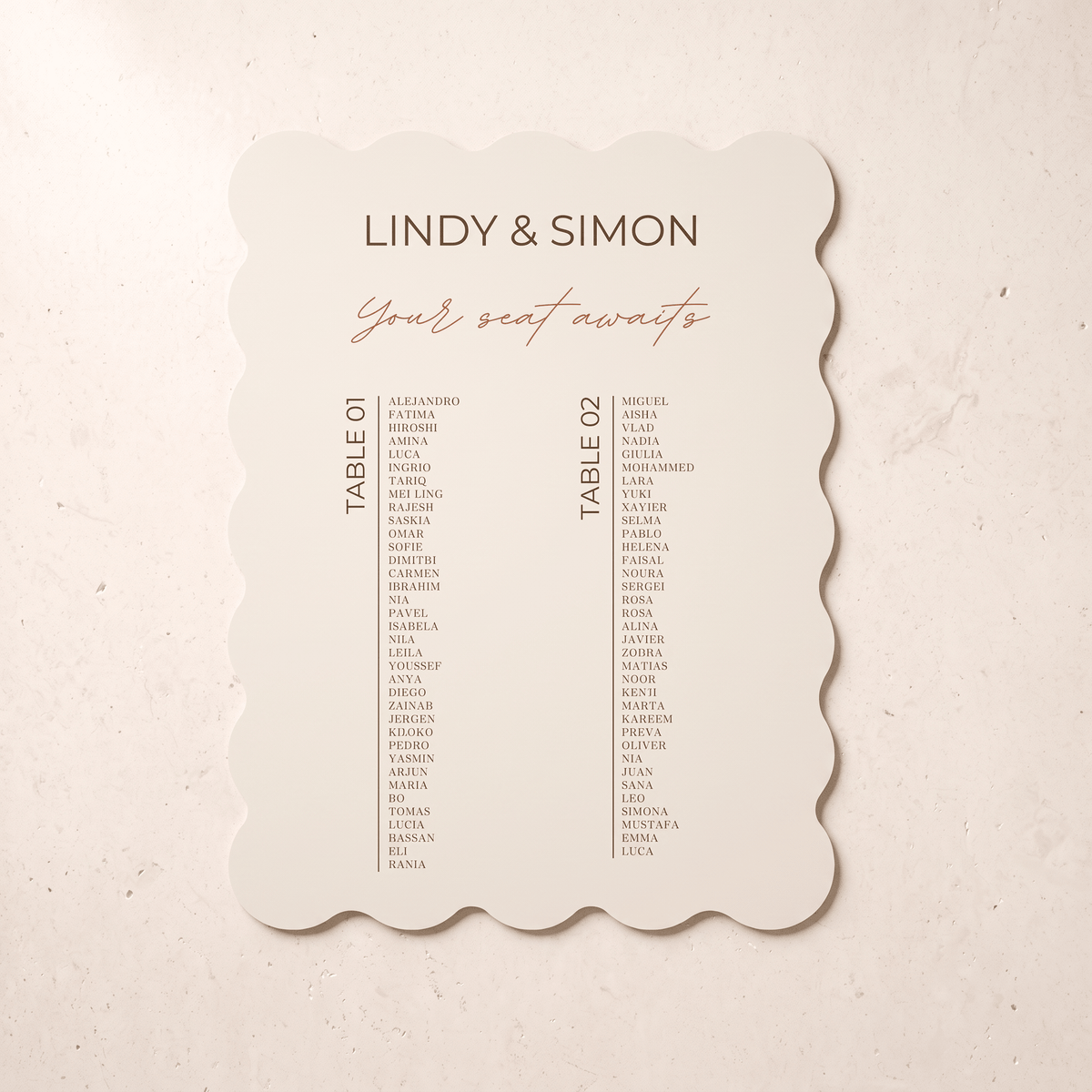 A scalloped-edge wedding seating card with the names of guests listed under table headings, photographed flat against a light beige textured background.