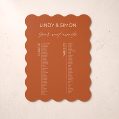 A scalloped terracotta orange wedding seating card with white printed text, displayed flat against a textured beige background.