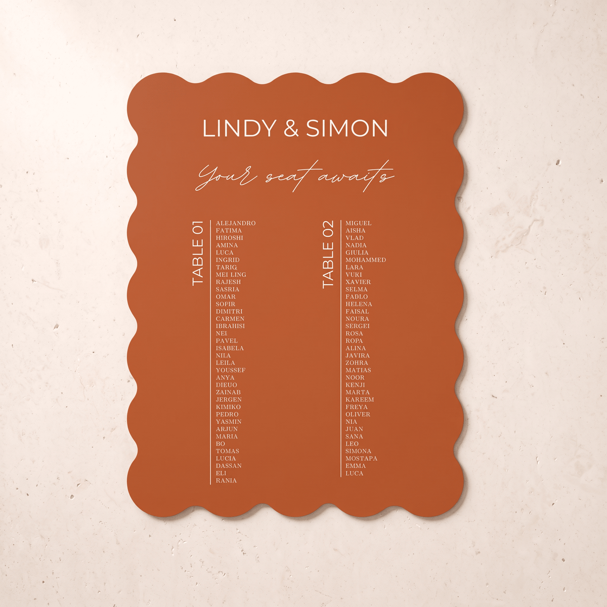 A scalloped terracotta orange wedding seating card with white printed text, displayed flat against a textured beige background.