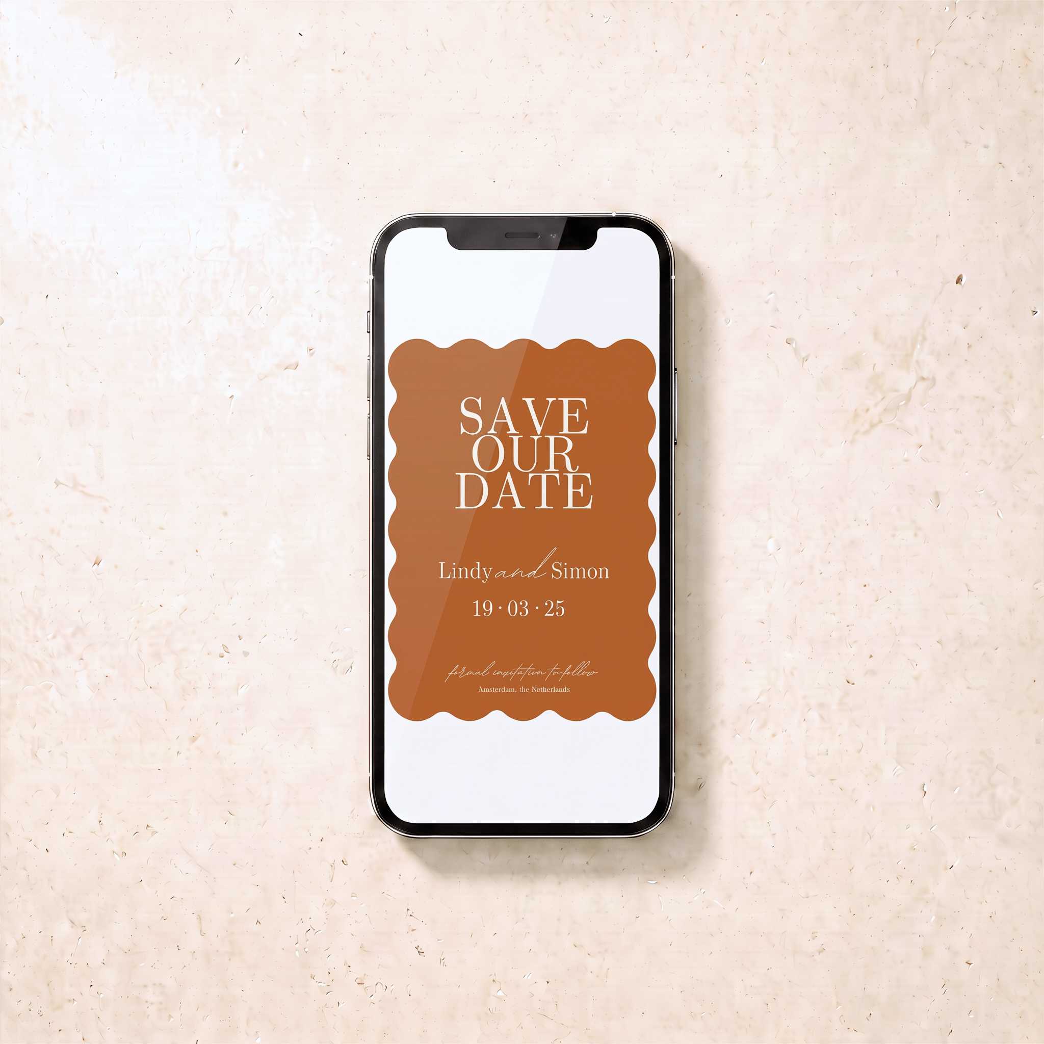 A smartphone lying on a light beige textured surface, displaying a brown and white 'Save Our Date' invitation design with scalloped edges and wedding text.