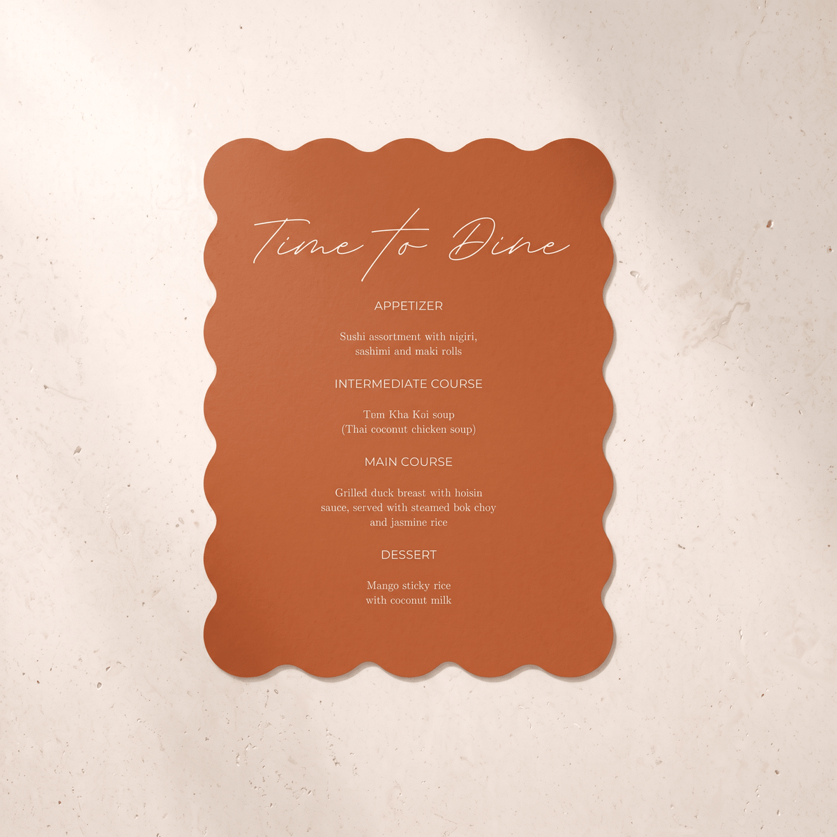 A scalloped terracotta orange menu card with white script and text reading 'Time to Dine' and course listings, photographed against a light beige textured background.